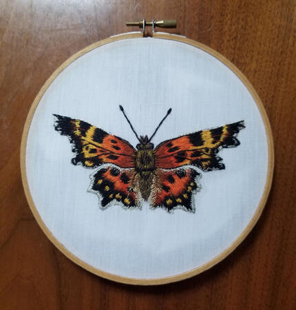 An embroidered piece of a green comma butterfly, using thread painting technique to give it a realistic appearance.